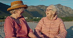 Senior women, happy and conversation on beach, bonding and laughing or relaxing on holiday. Elderly friends, care and humor in nature for support in retirement, funny joke and talking in outdoors