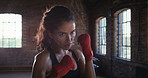 Strong, determined woman boxing during her cardio workout at the gym. A confident, focused athlete hitting a punching bag during her exercise routine. A powerful young Hispanic woman boxing at the gym