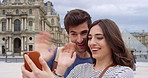 A happy young couple waving during a video call made on their cellphone in front of the Louvre