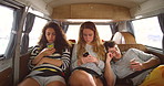 A group of young friends sitting in the back of a van during a roadtrip using their smartphones