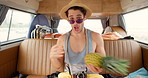 A young man having fun playing with a pineapple while taking photos in his camper van on vacation