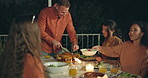 Friends, night and man cutting chicken on patio, happy or talking for food at new years eve celebration. Women, group and party at table for chat, memory or giving plate for salad, diversity or event