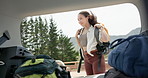 Happy woman, forest and unpacking car for backpack, hiking or travel on outdoor adventure. Female person, tourist or hiker getting bag from vehicle trunk for trekking, camping or journey in nature