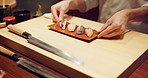 Hands, sushi plate and presentation in restaurant on table at diner, cuisine or expert cooking in night. Person, kitchen or fish with catering, ready and service for nutrition, diet or snack in Japan