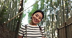 Woman, face and happy in bamboo forest for travel adventure, hiking and relax for journey, nature and park. Portrait, smile and Japanese tourist in jungle, environment or freedom in woods for holiday