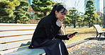 Happy asian woman, phone and relax on park bench for social media, communication or networking. Female person sitting with smile on mobile smartphone for online search, streaming or reading in nature