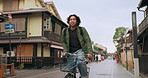 Bicycle, cycling and man by buildings for travel, exercise or transportation to college academy. Fitness, backpack and young male student driving a bike to university for carbon footprint by houses.