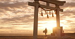 Torii gate, sunset sky and man at ocean with surfboard, spiritual history and travel adventure in Japan. Shinto architecture, Asian culture and calm beach in Japanese nature with sacred monument.