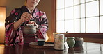 Traditional Japanese woman, pot and tea cup for health, wellness or liquid to relax at tearoom table. Girl, person and hands with drink for culture, detox and indigenous clothes with peace in home