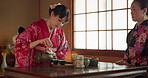 Culture, teapot and Asian women with tea with traditional herbs, leaves and wellness in home. Friends, ceremony and people with herbal beverage for relaxing, calm and detox for drinking ritual