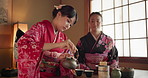 Pouring, teapot and Asian women with tea for culture with traditional leaves and herbs in home. Friends, ceremony and people with herbal beverage for relaxing, calm and detox for drinking ritual