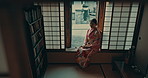 Thinking, window and traditional Asian woman with smile for reflection, calm and relaxing in morning. Kimono, culture and person in home with view for thoughtful, wondering and happy in living room