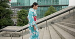 Japanese woman, happy and walking on stairs in kimono, travel and wellness on steps for peace attitude in city. Person, calm or traditional clothes by urban town buildings or journey in tokyo culture