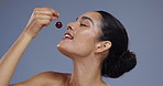 Skincare, eating cherry and face of woman on blue background for wellness, beauty and cosmetics. Dermatology, spa and portrait of person with fruit for nutrition, organic and natural detox in studio