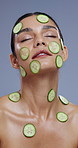 Face, cucumber on skin and woman with natural beauty, vegan or eco friendly product with wellness for skin in studio. Zen, detox and green fruit, self care with cosmetics and calm on grey background