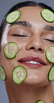 Woman, face and smile with cucumber in studio for organic treatment, anti aging or natural cosmetics. Model, vegetable and happy with dermatology for detox, healthy skin and beauty on gray background