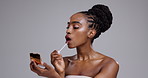 Woman, face and smile with lip gloss in studio for glowing skin, wellness and cosmetics with mirror. African model, person and mockup for facial treatment, lips care or skincare with gray background