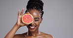 Grapefruit, beauty and face of happy woman in studio for vitamin c benefits, detox or glow on grey background. Portrait, african model or laugh with citrus fruits for skincare, sustainability or diet