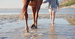 Beach, feet and woman with a horse walking to water in nature for travel, adventure and trip. Island, resort and legs of  female person with stallion at the ocean for sundown fun, freedom or holiday