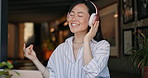 Happy asian woman, headphones and listening to music in cafe for audio streaming, dancing or singing. Female person or freelancer smile or enjoying podcast, sound or song at coffee shop or restaurant