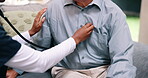 Hands, medical and stethoscope on chest of old man in living room of home for appointment or checkup. Healthcare, consulting and breathing with nurse listening to heartbeat of patient in apartment