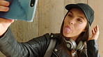 A young woman on holiday pulling funny faces and taking selfies on her smartphone in front of a wooden wall. A young student taking selfies on her cellphone by a wood wall before going to university