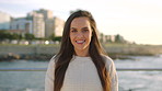 A happy young woman smiling on the promenade at sunset during her holiday. Smiling woman on vacation at the beach enjoying the sunrise. Smiling young woman on the beach enjoying the sunset