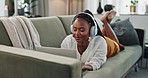Home, headphones and black woman on a couch, laptop and typing with connection, internet and streaming music. African person, apartment and girl on a sofa, pc and headset with sound, song and audio