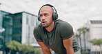 Fitness, fatigue and man with headphones in city to relax with audio, streaming and challenge. Workout, breathing and tired urban runner on break listening to music, podcast or exercise app in street