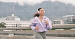 Fitness, running and woman in a city for training, sport and wellness with music for motivation on a bridge. Runner, girl and run workout with energy, speed and intense practice with podcast 
