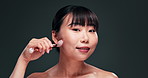 Beauty, laughing and jade roller for face with asian woman in studio on dark background for skincare or wellness. Portrait, massage or funny and happy young person with product for dermatology