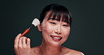 Face, cosmetics and Japanese woman with makeup brush and aesthetic on dark studio background. Person, girl or model with shine and glowing with wellness or treatment with skincare, smile and grooming