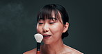 Makeup, brush and face of happy woman in studio for cosmetics, treatment or application on black background. Beauty, tool and portrait of playful Japanese model blowing powder, foundation or product