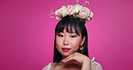 Touch face, beauty and Asian woman with flower crown on pink background for wellness, confidence and skincare. Luxury salon, floral aesthetic and portrait of person for natural cosmetics in studio