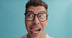 Happy man, face and glasses of geek or nerd with silly facial expression on a blue studio background. Closeup of young male person, goofy or smart model with spectacles or tongue out on mockup space