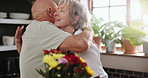 Hug, flowers and home with old couple, gift and kissing with anniversary and celebration with marriage. Kitchen, elderly man and senior woman with a present and surprise with romance and relationship