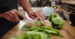 Person, hands and cutting cucumber with knife on board for food preparation or healthy meal in the kitchen. Closeup of chef or cook slicing natural and organic green vegetables for salad at home