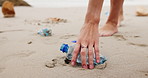 Person, hands and beach with plastic bottle for recycling, cleaning or saving the planet in nature. Closeup of volunteer picking up rubbish, dirt or garbage of waste on the sandy shore or ocean coast