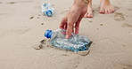 People, hands and beach with plastic bottle for recycling, cleaning or saving the planet in nature. Closeup of volunteer picking up rubbish, dirt or garbage in bag on the sandy shore or ocean coast