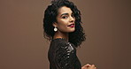 Portrait, hair and fashion with woman in makeup, wink in sparkle dress and cosmetics on brown background. Flirt, face with red lipstick and haircare, curly hairstyle and stylish clothes in studio