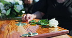 Flower, coffin and hands of person at funeral for death ceremony, graveyard and memorial service. Pain, closeup and rose on gravestone for mourning, burial or loss in public cemetery for farewell