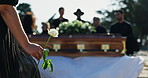 Person, hand and rose with coffin at cemetery for death, Christianity or grief in ceremony of loss. Closeup of woman holding flower at funeral for respect, emotion or blessing by graveyard or casket