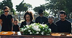 Family, sad and coffin at graveyard for funeral, service and burial ceremony with flower bouquet. Death, grief and people at cemetery with casket for loss, mourning and depression at memorial