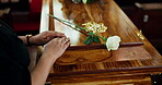 Coffin, flower and hands of widow at funeral for goodbye with grief, loss or pain of mourning closeup. Sad, death and rose for respect with person in church for farewell ceremony or memorial service