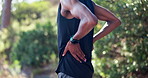 Hands, black man and back pain from exercise in outdoor with muscle stretch on workout or jogging in forest. Male person, runner and active with injury from fitness and check damage for health