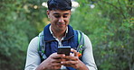 Phone, nature and man hiking in woods networking on social media, mobile app or internet. Smile, technology and male person typing on cellphone trekking in outdoor forest for exploring or adventure.