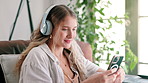Phone, headphones and woman on sofa at house networking on social media, mobile app or internet. Smile, typing and female person listening to music, radio or album on cellphone in living room at home