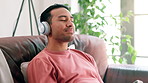 Relax, headphones and man on sofa at his home listening to music, playlist or radio online. Smile, rest and calm male person streaming album or song on cellphone in living room at modern apartment.