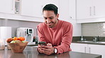 Phone, typing and happy man on table in kitchen at home for social media, network or reading email on technology. Smartphone, scroll or smile of person on internet, website or mobile app in apartment