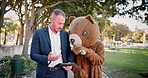 Business people, tablet and discussion of team outdoor at park in funny teddy bear costume. Technology, meeting and collaboration of consultants planning, brainstorming or walk with mascot in garden